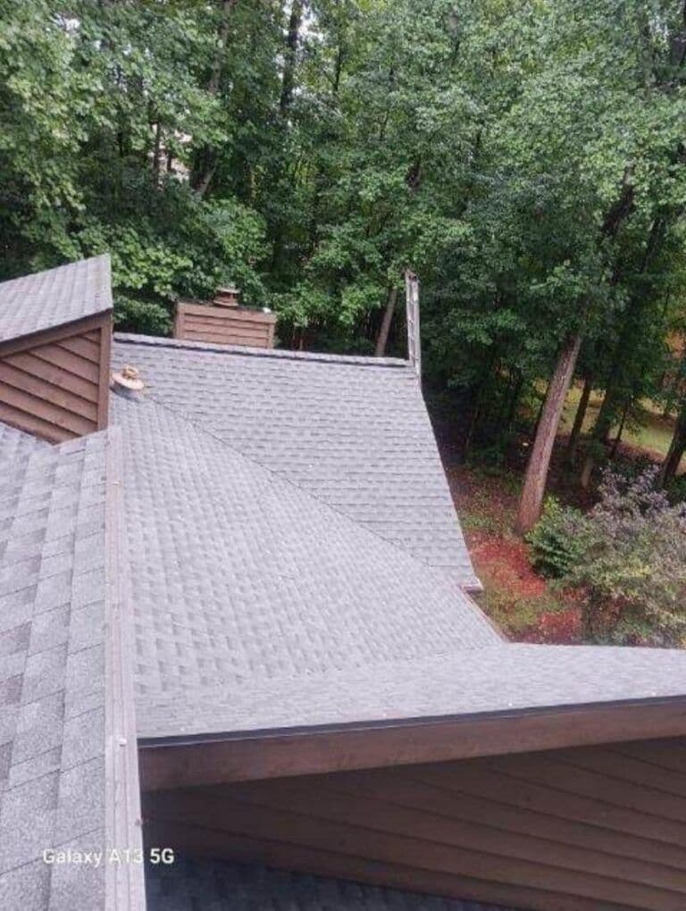 View from above shows a gray, shingled rooftop in a forested area. Trees surround the house, creating a calm, natural atmosphere.