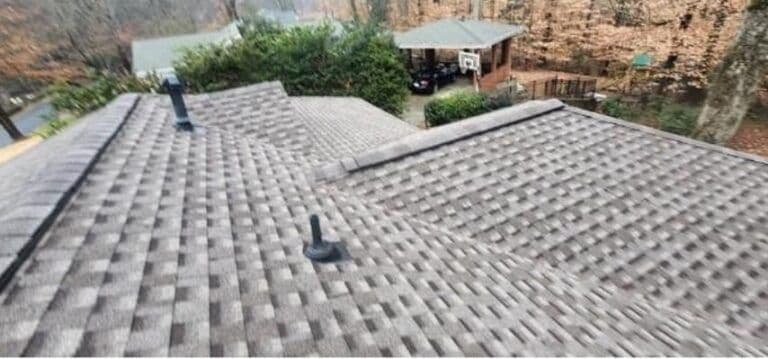 Aerial view of a house's shingled roof with two black vents. In the background, there's a garden, gazebo, basketball hoop, and autumn trees.