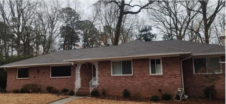 A single-story brick house with gray roof shingles, surrounded by bare trees and withered grass, evokes a quiet, wintry suburban atmosphere.