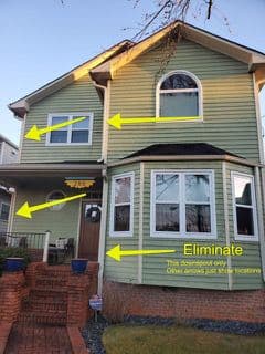 Two-story green house with brick steps and yellow arrows pointing to features. Text reads: "Eliminate this downspout only." Bright, clear day.
